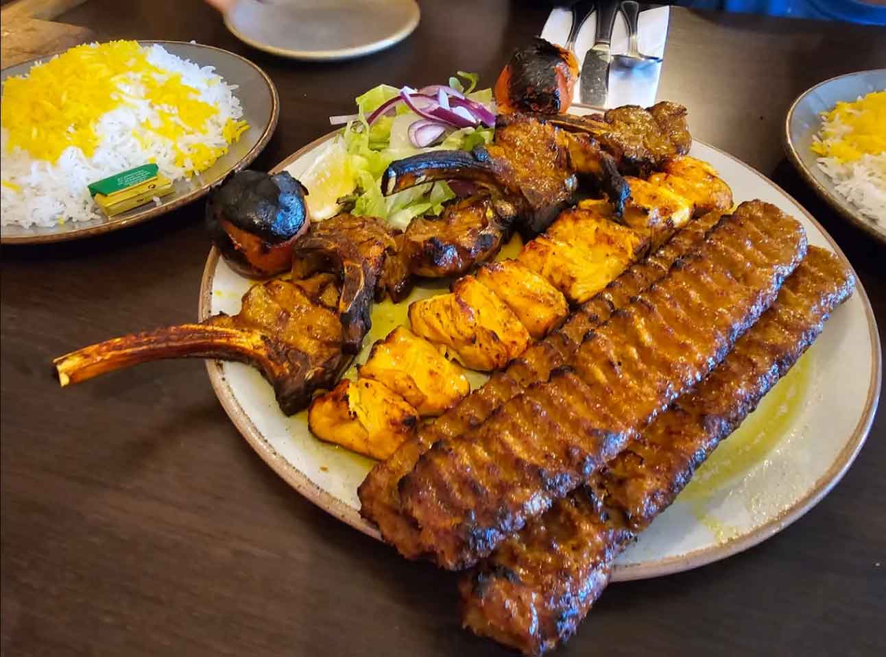 A plate of Persian mixed kebabs includes lamb chops, chicken, and koobideh.